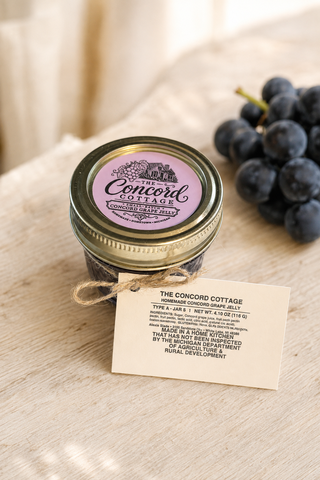 Small Concord grape jelly jar with a purple lid label beside homegrown grapes